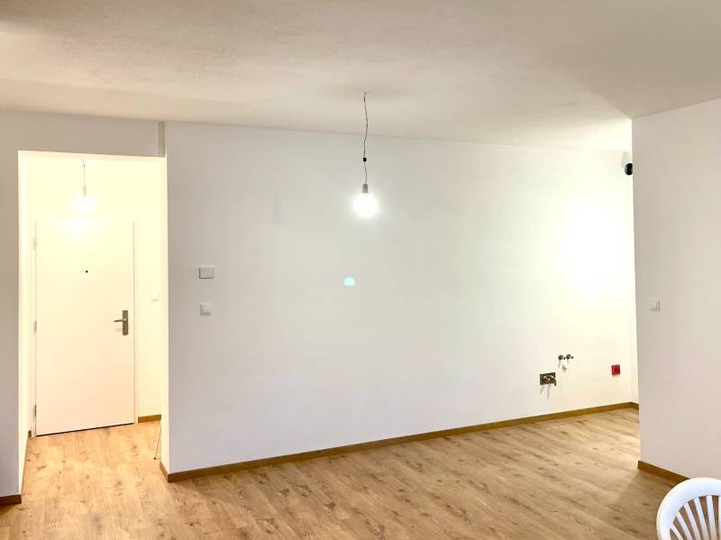 I Predaj 3i bytu v novostavbe v Rači - Prázdna miestnosť s bielymi stenami, podlaha s dreveným dekorom, dve žiarovky visiace zo stropu.