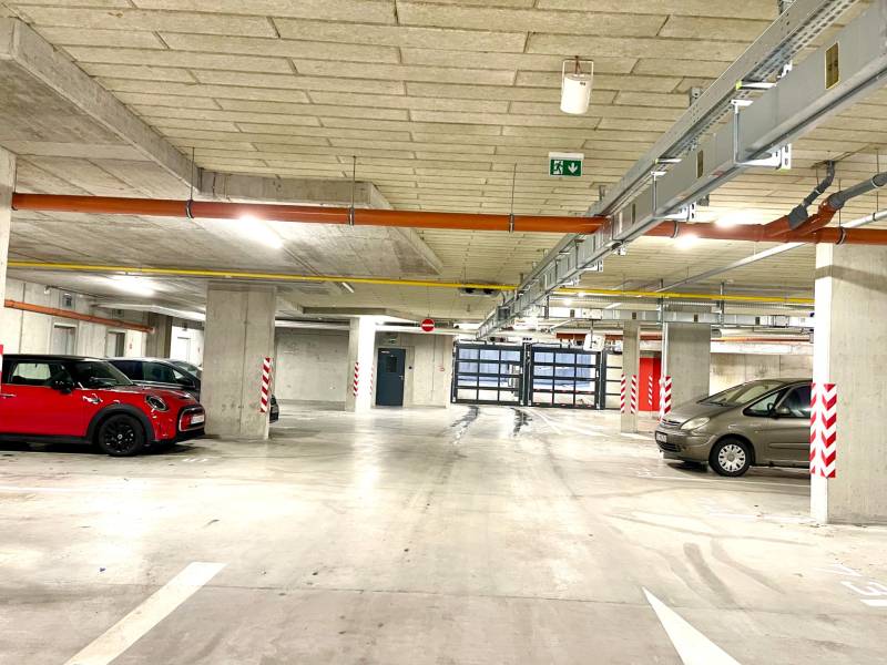 I Predaj 3i bytu v novostavbe v Rači - Podzemné parkovisko s parkovanými autami a pruhovanými stĺpmi, betónová konštrukcia, jasné osvetlenie.