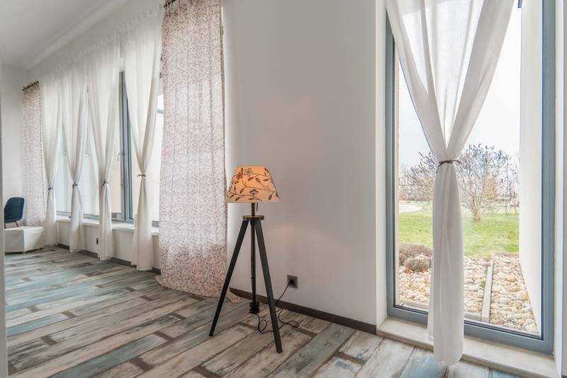 I PREDAJ moderná vila s bazénom a veľkým pozemkom - Interiér Vily s podlahou s dreveným dekorom, veľkými oknami a stojacou lampou.