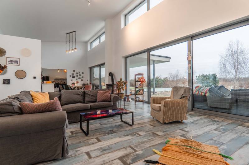 I PREDAJ moderná vila s bazénom a veľkým pozemkom - Priestranný interiér vily s veľkými oknami a pohodlným nábytkom, podlaha s dreveným dekorom.