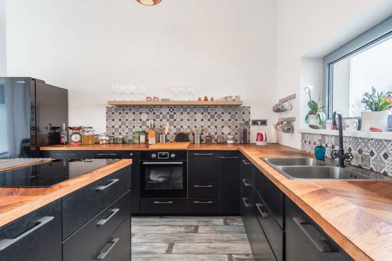 I PREDAJ moderná vila s bazénom a veľkým pozemkom - Kuchyňa vo vile s čiernymi skrinkami, dekoratívnym obkladom a podlahou s dreveným dekorom.