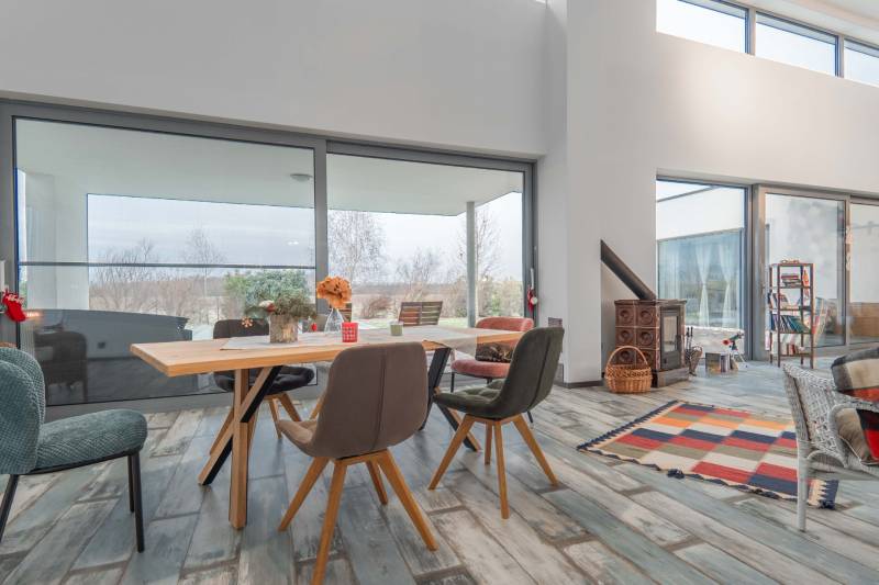 I PREDAJ moderná vila s bazénom a veľkým pozemkom - Interiér Vily s podlahou s dreveným dekorom, jedálenským stolom a veľkými oknami.