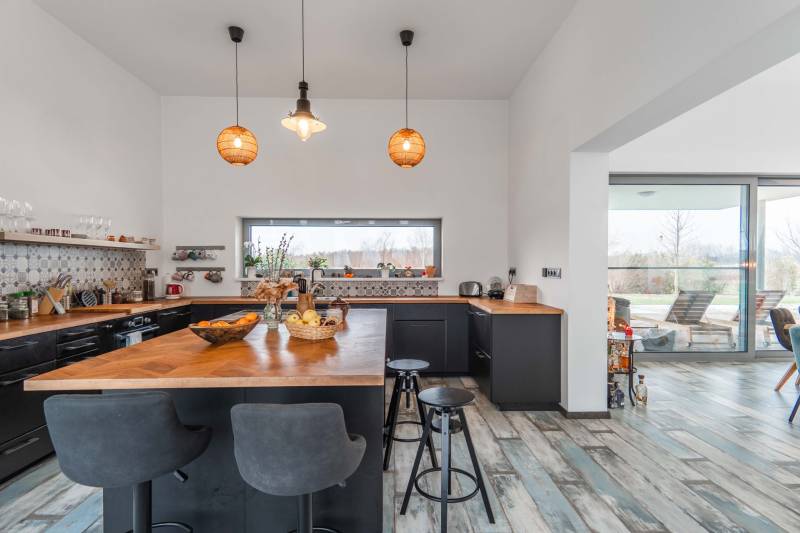 I PREDAJ moderná vila s bazénom a veľkým pozemkom - Kuchyňa vo vile s dreveným dekorom, barovými stoličkami a závesným osvetlením.
