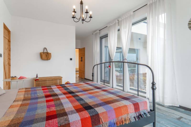 I PREDAJ moderná vila s bazénom a veľkým pozemkom - Spálňa s kovovou posteľou, pestrofarebným prehozom, závesmi a podlahou s dreveným dekorom v rodinnom dome.