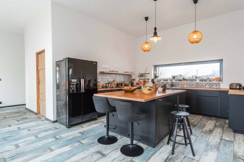 I PREDAJ moderná vila s bazénom a veľkým pozemkom - Kuchyňa vo vile s dreveným dekorom, čiernym nábytkom a centrálnym ostrovom.