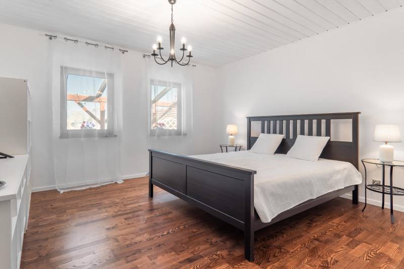 Stavebný pozemok 8 500 m² s podnikateľským potenciálom - Spálňa s posteľou, podlahu zdobí drevený dekor, svetelný luster, záclony na oknách.
