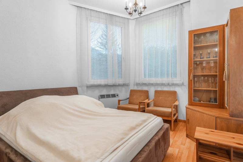 I Predaj bytu v Semmeringu, Rakúsko – výborná investícia - Jednoizbový byt so spálňou, podlahou s dreveným dekorom, stoličkami a presklenou vitrínou.
