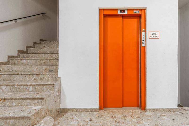 I Predaj bytu v Semmeringu, Rakúsko – výborná investícia - Oranžový výťah a schodisko s kamennými schodmi v budove.