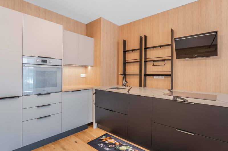 : Nadštandardný 2-i byt v projekte ZWIRN za cenu „štandardu“ - Kuchyňa v 2-izbovom byte s drevenými prvkami, vstavanou rúrou a sivými skrinkami.