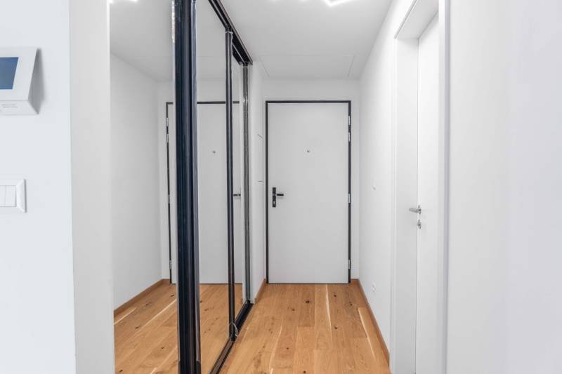 : Nadštandardný 2-i byt v projekte ZWIRN za cenu „štandardu“ - Chodba v 2-izbovom byte s drevenou podlahou a bielymi stenami.