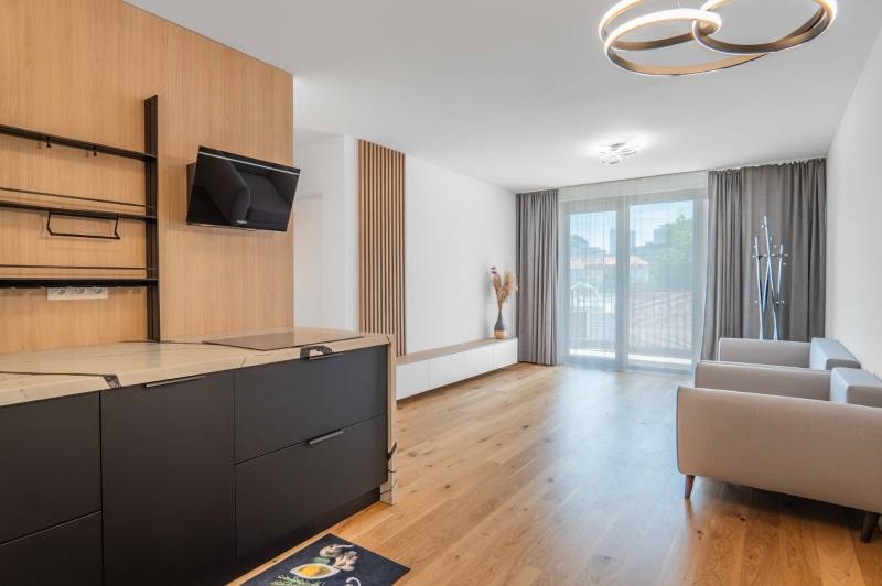 : Nadštandardný 2-i byt v projekte ZWIRN za cenu „štandardu“ - Obývacia izba v 2-izbovom byte s drevenou podlahou a vstavanou kuchyňou.