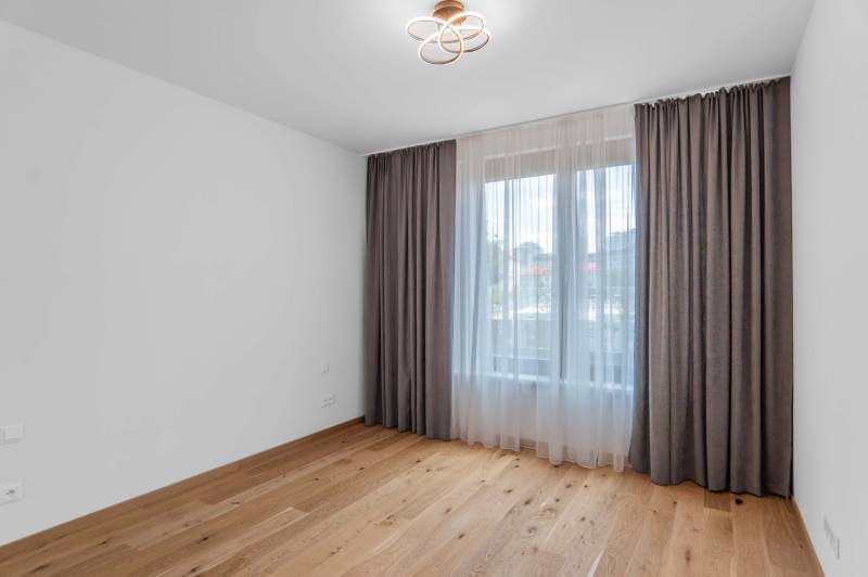 : Nadštandardný 2-i byt v projekte ZWIRN za cenu „štandardu“ - Izba s drevenou podlahou a veľkým oknom so závesmi v 2-izbovom byte.