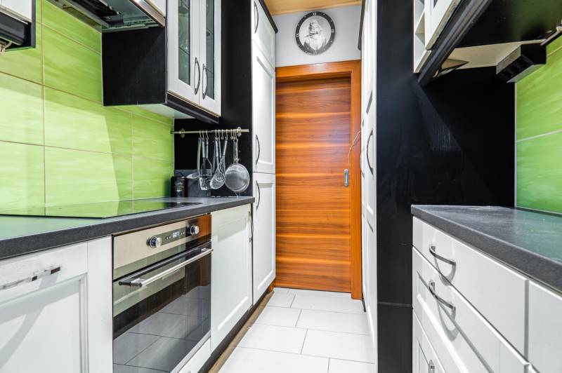 I Na predaj 2-i byt s terasou v Auersthal (Rakúsko) - Úzka kuchyňa s bielymi skrinkami, čiernymi pracovnými doskami a zelenými obkladačkami v 2-izbovom byte.