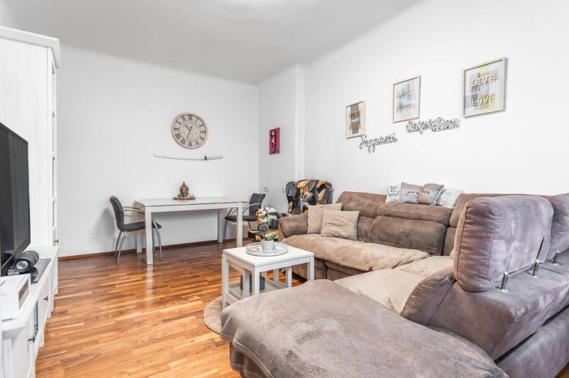 I Na predaj 2-i byt s terasou v Auersthal (Rakúsko) - Obývačka 2-izbového bytu s podlahou s dreveným dekorom, pohovkou a jedálenským kútom.