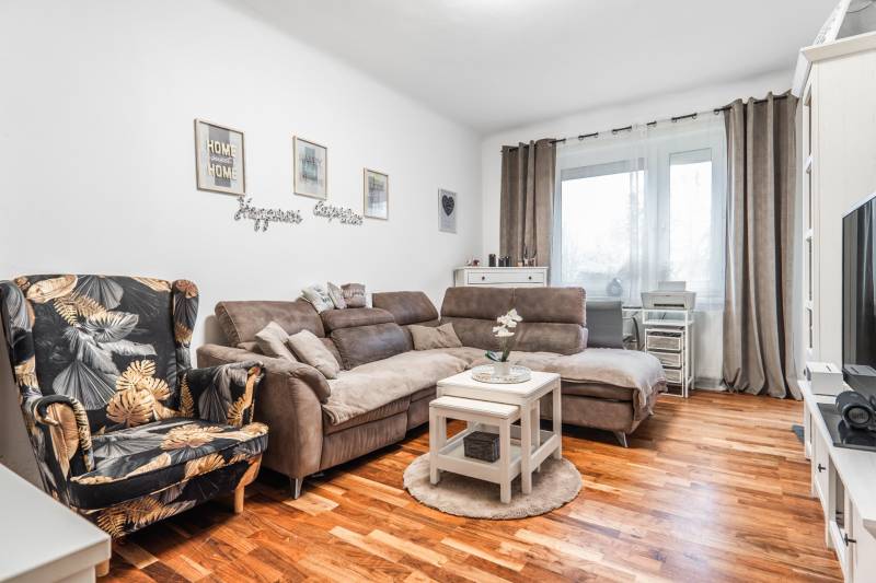 I Na predaj 2-i byt s terasou v Auersthal (Rakúsko) - Svetlá obývačka v 2-izbovom byte s pohovkou, kreslom a podlahou s dreveným dekorom.