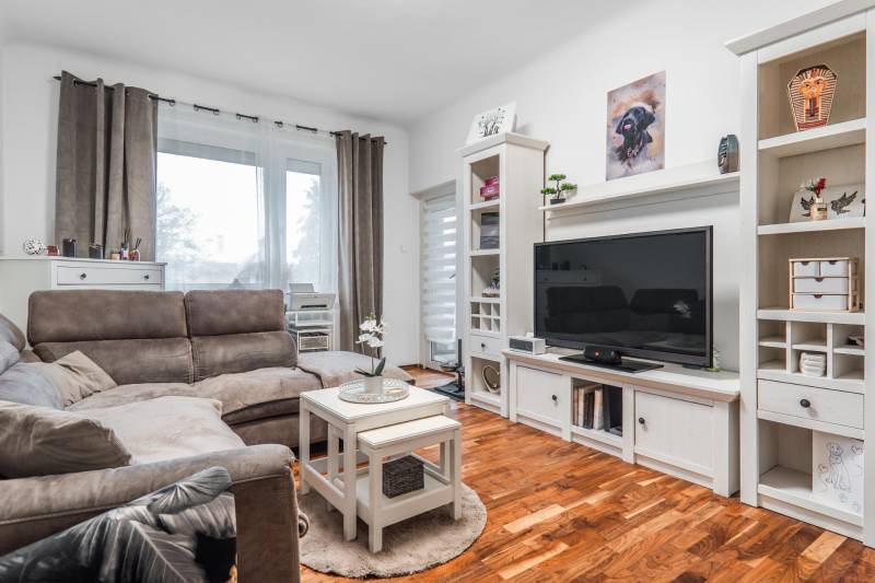 I Na predaj 2-i byt s terasou v Auersthal (Rakúsko) - Obývacia izba v 2-izbovom byte s pohovkou, televízorom a podlahou s dreveným dekorom.