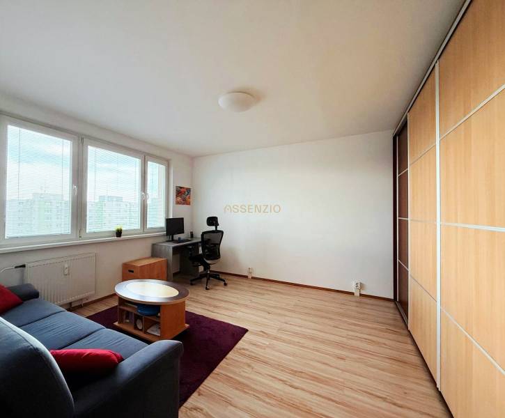 - PRENÁJOM - 1 IZBOVÝ BYT - TOPOĽČIANSKA UL. - PETRŽALKA - Svetlá obývačka s pracovným stolom, gaučom a podlahou s dreveným dekorom v 1-izbovom byte.