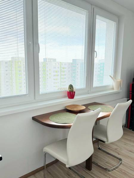 - PRENÁJOM - 1 IZBOVÝ BYT - TOPOĽČIANSKA UL. - PETRŽALKA - Stolík so židlemi pri okne v 1-izbovom byte s podlahou s dreveným dekorom.