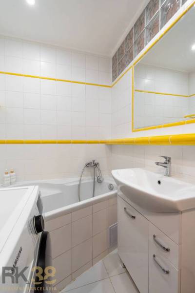 Exkluzívny byt v srdci Vysokých Tatier na Štrbskom Plese - Kúpeľňa Rekreačného apartmánu s vaňou, umývadlom, práčkou a bielymi obkladmi.