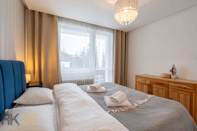 Exkluzívny byt v srdci Vysokých Tatier na Štrbskom Plese - Spálňa v rekreačnom apartmáne s manželskou posteľou a komodou, okno s výhľadom.