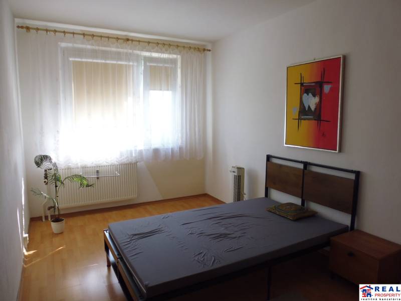 PRENÁJOM: M.NEŠPORA - 2-izbový byt, 58 m2, 7.posch. - Sídlisko III. - Štýlová spálňa v 2-izbovom byte s podlahou s dreveným dekorom a umeleckým obrazom.