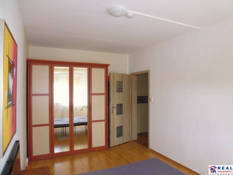 PRENÁJOM: M.NEŠPORA - 2-izbový byt, 58 m2, 7.posch. - Sídlisko III. - Interiér 2-izbového bytu s veľkou zrkadlovou skriňou a podlahou s dreveným dekorom.