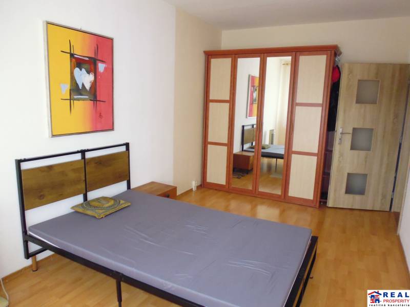 PRENÁJOM: M.NEŠPORA - 2-izbový byt, 58 m2, 7.posch. - Sídlisko III. - Spálňa s posteľou, podlahou s dreveným dekorom a skriňou v 2-izbovom byte.