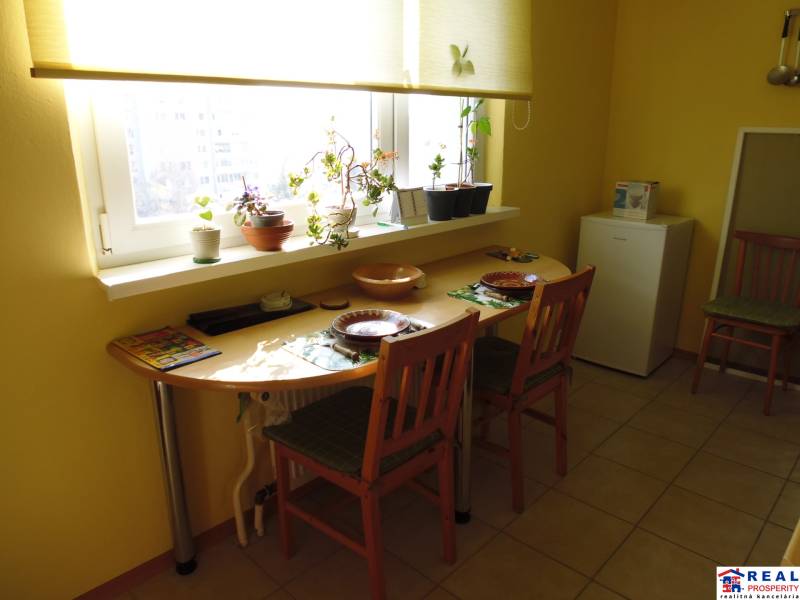 PRENÁJOM: M.NEŠPORA - 2-izbový byt, 58 m2, 7.posch. - Sídlisko III. - Jedálenský kút v 2-izbovom byte s oknom a rastlinami na parapete.