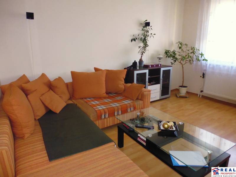 PRENÁJOM: M.NEŠPORA - 2-izbový byt, 58 m2, 7.posch. - Sídlisko III. - Obývacia izba v 2-izbovom byte s oranžovou sedacou súpravou a podlahou s dreveným dekorom.