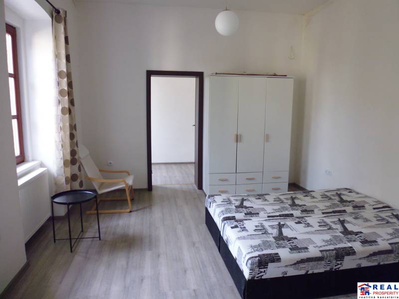 PRENÁJOM: HLAVNÁ - VOĽNÝ 2,5-izbový byt + kuchyňa, kúpeľňa, WC  - Spálňa v 3-izbovom byte s podlahou s dreveným dekorom, skriňou a posteľou.