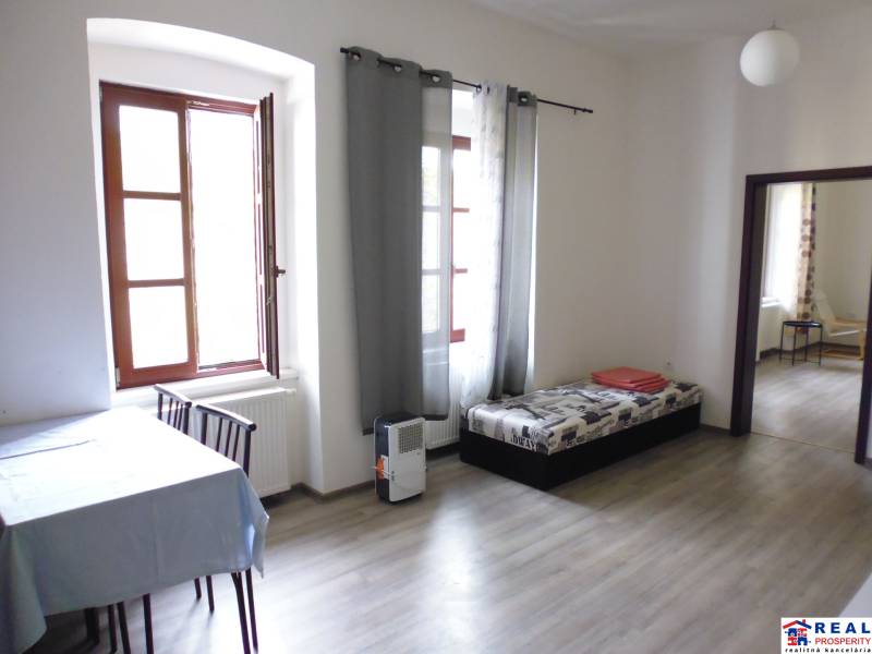 PRENÁJOM: HLAVNÁ - VOĽNÝ 2,5-izbový byt + kuchyňa, kúpeľňa, WC  - Obývacia izba so stolom a pohovkou v 3-izbovom byte, podlaha s dreveným dekorom.