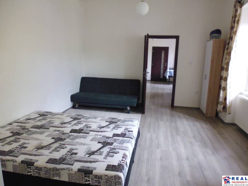 PRENÁJOM: HLAVNÁ - VOĽNÝ 2,5-izbový byt + kuchyňa, kúpeľňa, WC  - Spálňa v 3-izbovom byte s posteľou, pohovkou a podlahou s dreveným dekorom.