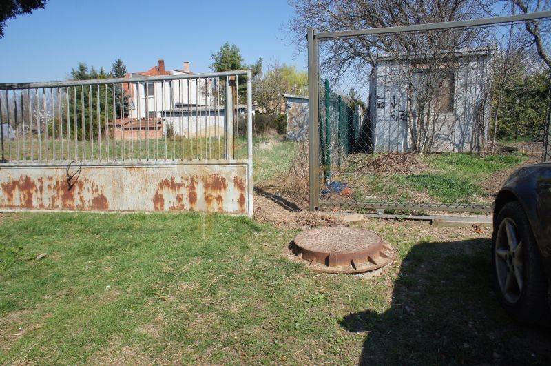 Pozemok v obci Koniarovce v slepej uličke - Brána vedúca na pozemok so stavbou a trávnatou plochou, ideálne pre bývanie.