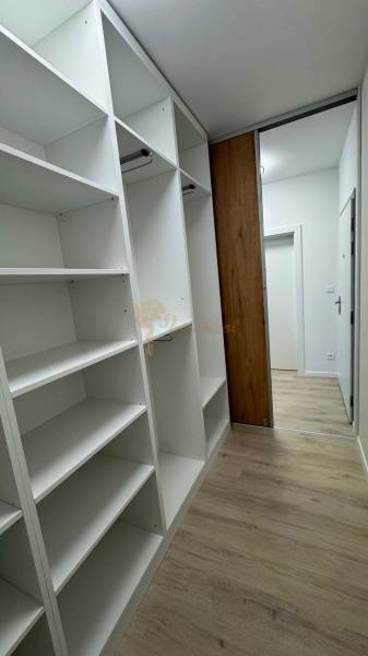 Novostavba 2,5-izb. bytu v NUPPU, garážové státie + vonkajšie státie - Biela vstavaná skriňa s policami a závesmi v 2-izbovom byte, podlaha s dreveným dekorom.