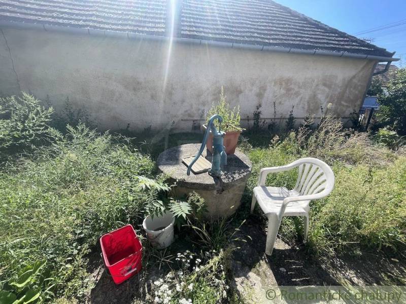 Trojizbový rodinný dom vhodný aj na chalupu v kľudnej časti obce Jatov - Záhrada v Jatove s pumpou, plastovou stoličkou a vedrom pri rodinnom dome.