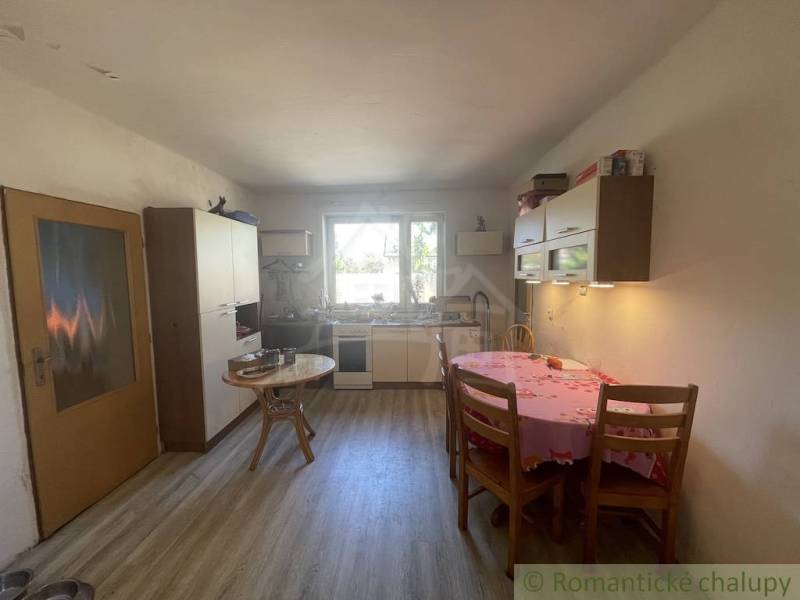 Trojizbový rodinný dom vhodný aj na chalupu v kľudnej časti obce Jatov - Kuchyňa v rodinnom dome s dreveným dekorom podlahy, jednoduchý nábytok a jedálenský stôl.