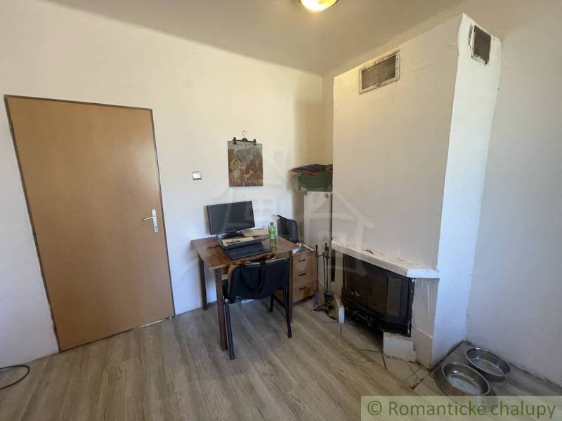 Trojizbový rodinný dom vhodný aj na chalupu v kľudnej časti obce Jatov - Interiér rodinného domu s krbom, pracovným stolom a podlahou s dreveným dekorom.