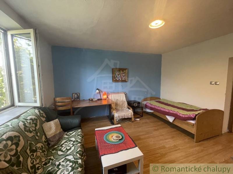 Trojizbový rodinný dom vhodný aj na chalupu v kľudnej časti obce Jatov - Izba v rodinnom dome s posteľou, oknom, sedačkou a podlahou s dreveným dekorom.