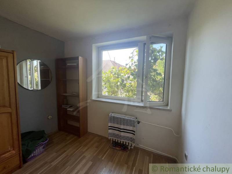 Trojizbový rodinný dom vhodný aj na chalupu v kľudnej časti obce Jatov - Izba v rodinnom dome s podlahou s dreveným dekorom, oknom a regálom.