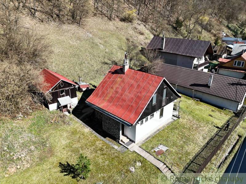 Chalupa - rodinný dom v krásnom prostredí – Moštenica, Banská Bystrica - Chata v Moštenici so šikmou červenou strechou, okolitá zeleň a svahovitý terén.