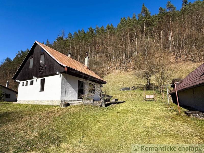 Chalupa - rodinný dom v krásnom prostredí – Moštenica, Banská Bystrica - Chata v Moštenici obklopená trávnatým pozemkom a lesom v pozadí.
