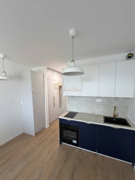 Garzónka v novostavbe AGÁTY, ul. Agátova, Dúbravka, lodžia  - Kuchyňa garsónky so svetlými skrinkami, sivou pracovnou doskou a podlahou s dreveným dekorom.