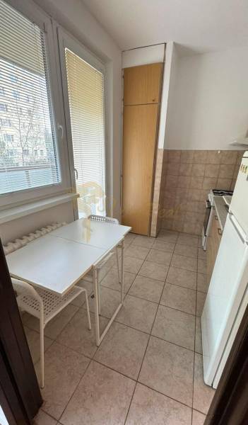 1-izb. byt, J.Stanislava, Karlova Ves, lodžia, 3.p./8 - Svetlá kuchyňa s oknom, jednoduchým stolom a stoličkami v 1-izbovom byte.