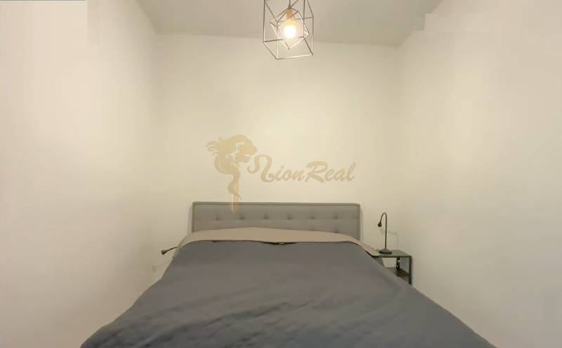 1,5 izb. byt s predzáhradkou, Podunajské Biskupice, projekt Oppidum - Spálňa v 2-izbovom byte so sivou posteľou a závesným svetlom.