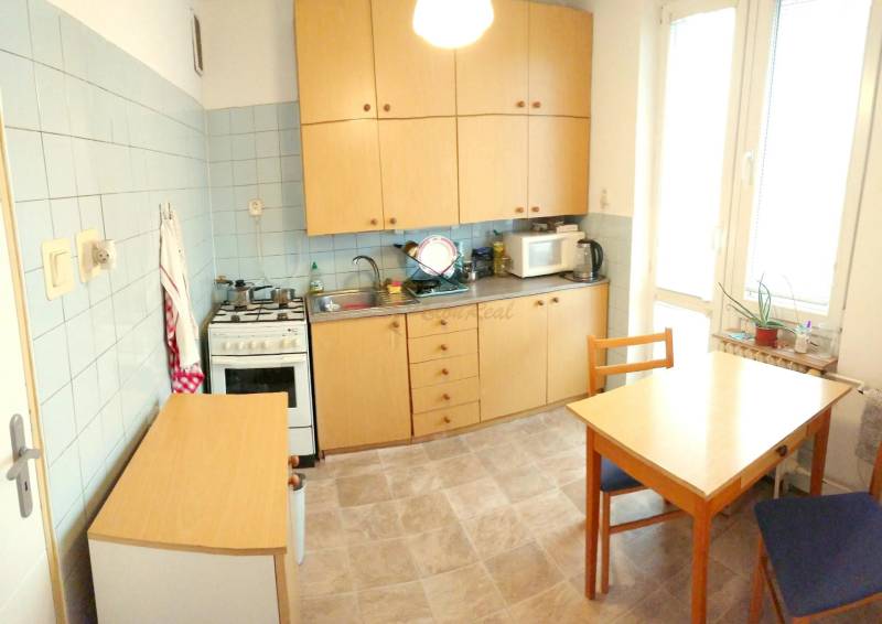 2-izb. byt pri Račianskom Mýte, balkón, 5.p./11 - Kuchyňa s jedálenským stolom a drevenými skrinkami v 2-izbovom byte.