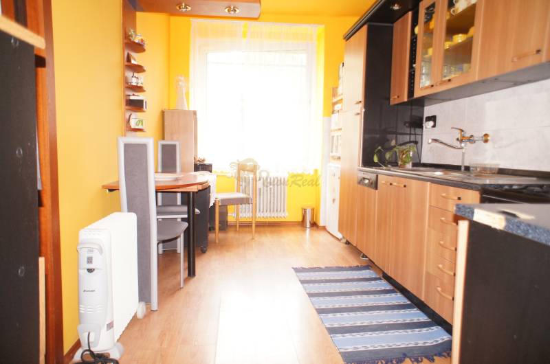 Veľký 1-izb. byt v tehlovom dome, Miletičova ul., Ružinov  - Kuchyňa v 1-izbovom byte s dreveným dekorom, jedálenským stolom a žltou stenou.