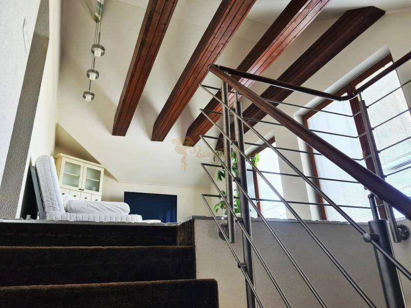 5-izb. dvojpodlažný rodinný dom, Rovinka - Interiér rodinného domu s modernými schodmi, drevenými trámami a kreslom pri okne.