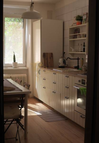 Veľký 2-izb. byt v tehlovom dome, Ružová dolina, Ružinov časť Nivy - Kuchyňa s jedálenským stolom, bielymi skrinkami a podlahou s dreveným dekorom v 2-izbovom byte.