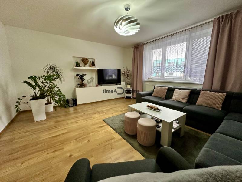 Na predaj: Priestranný rodinný dom v tichej lokalite obce Červeník - Obývačka v rodinnom dome s podlahou s dreveným dekorom, veľkou sedačkou a televíziou.