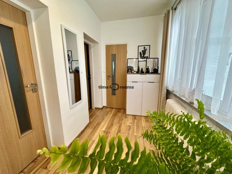 Na predaj: Priestranný rodinný dom v tichej lokalite obce Červeník - Interiér rodinného domu s podlahou s dreveným dekorom, bielou komodou a izbovou rastlinou.